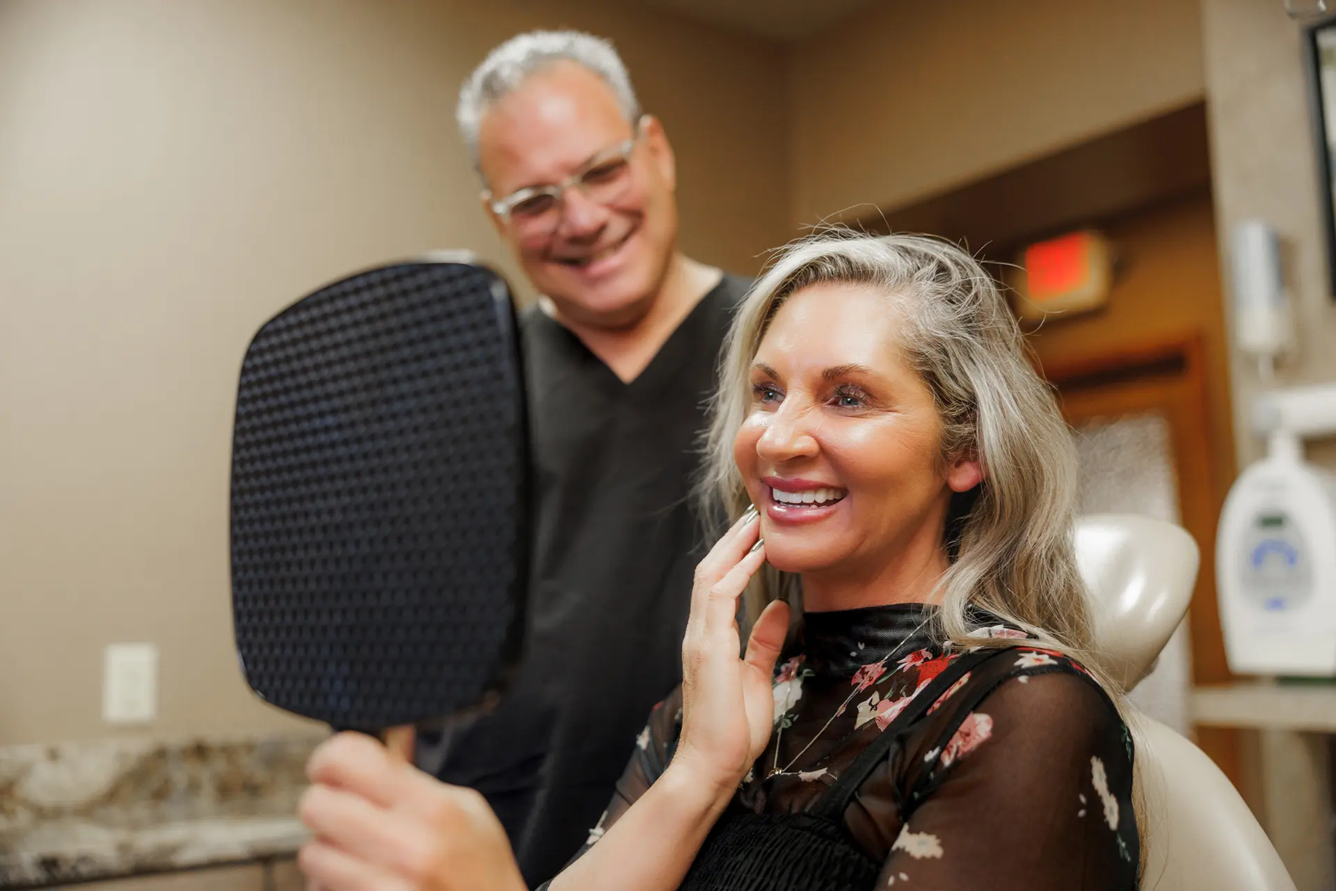A patient reviewing her new smile in a mirror at the Jirik DDS office